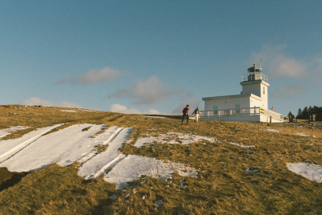 couple in wool sweaters run toward lighthouse