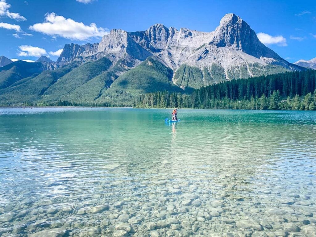 A couple paddleboarding on a clear blue lake with Mount Rundle in the background in Kananaskis, Alberta