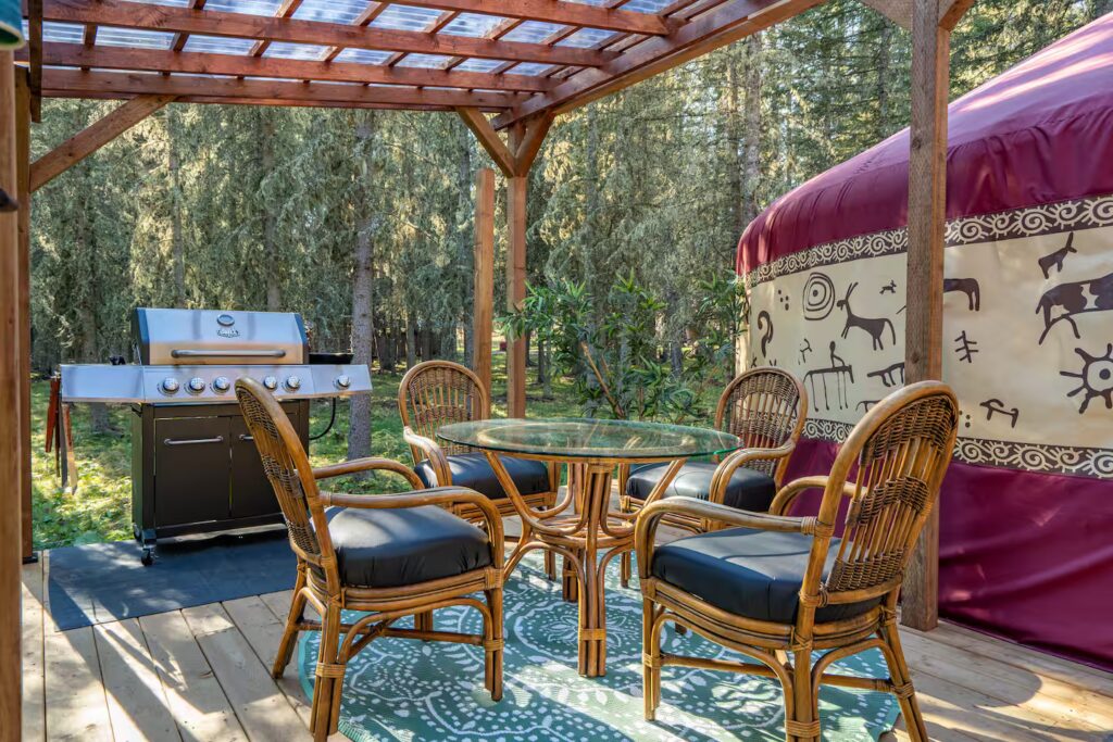 a patio beside a rustic yurt with a barbeque and patio furniture