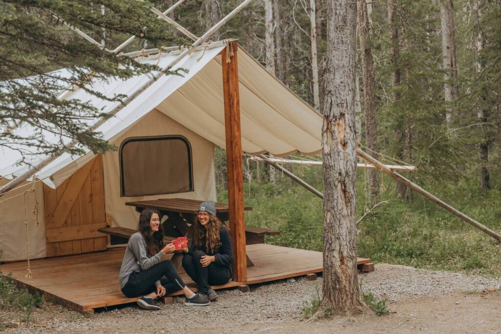 a couple drinks coffee in front of a glamping tent in the forest in Kananaskis, Alberta