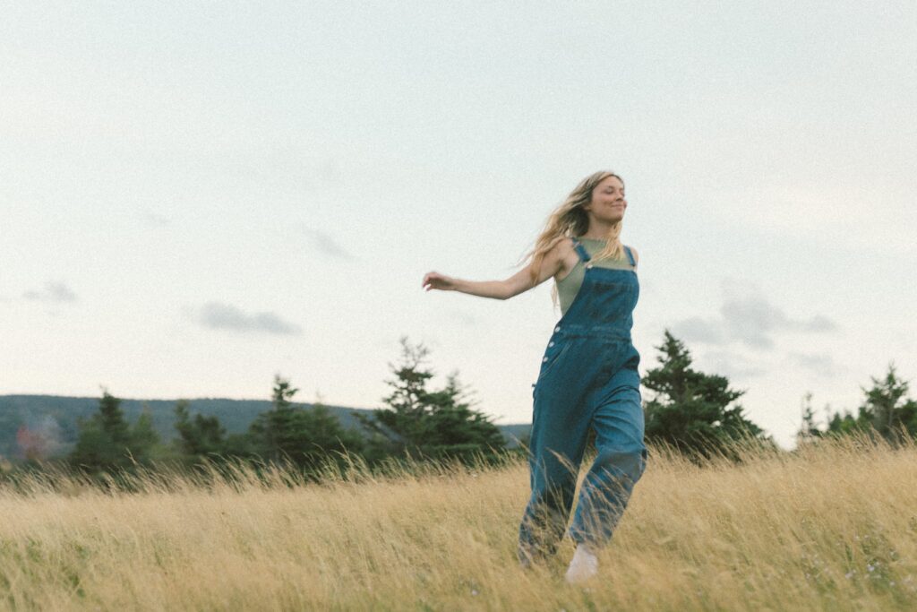 blonde woman runs through a field of tall grass at sunset during Self Love Session