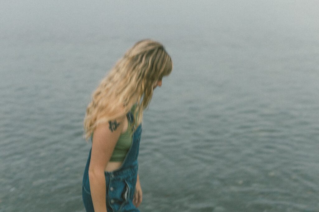 blonde woman with tattoos walks along the sea shore at sunset