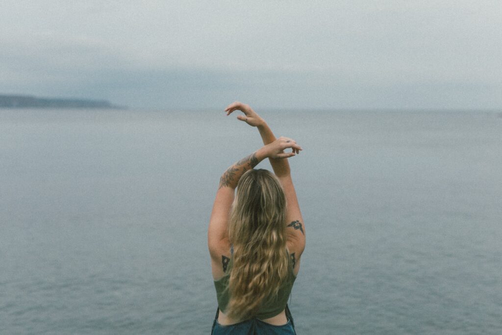 blonde woman with tattoos dances by the ocean at sunset during Self Love Session