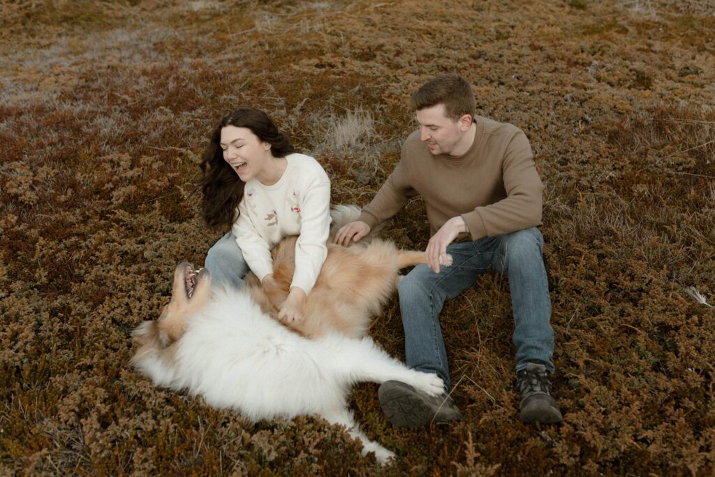 candid photo of a couple sitting in the grass petting their dog