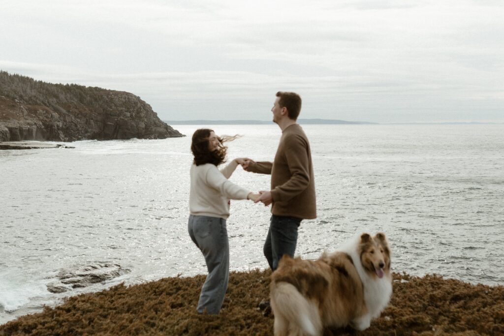 photo of a couple playfully dancing with their dog on a hill above the ocean