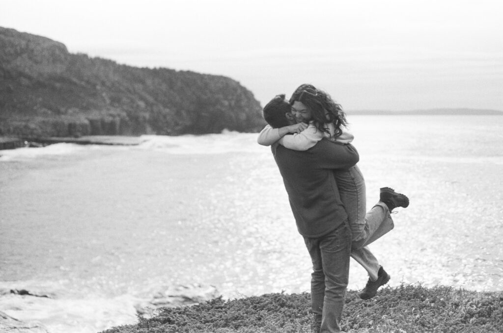 film photo of a woman jumping into a man's arms with the sun glinting on the ocean behind them