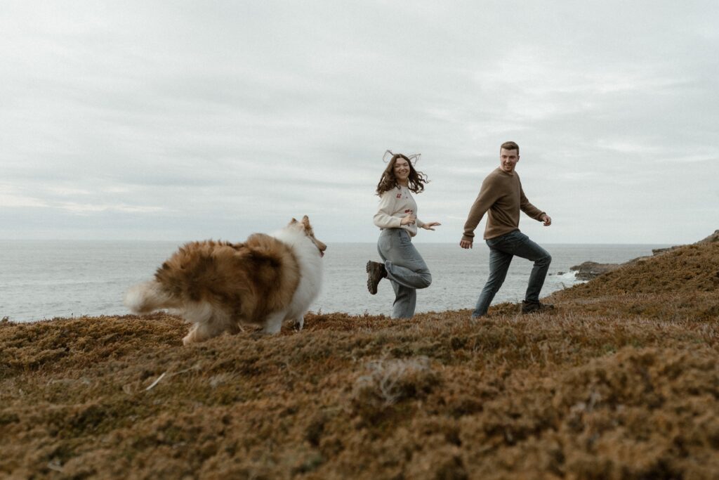 candid photo of a couple playing with their dog by the ocean