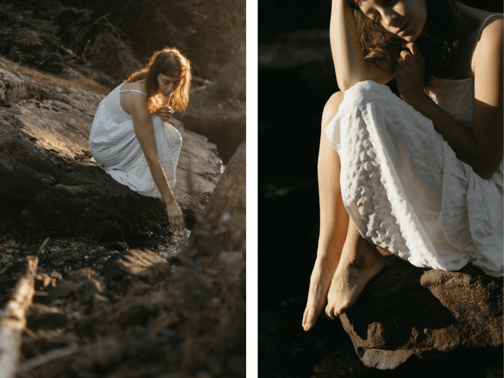 a woman in a long white dress bends down to put her hands in a river