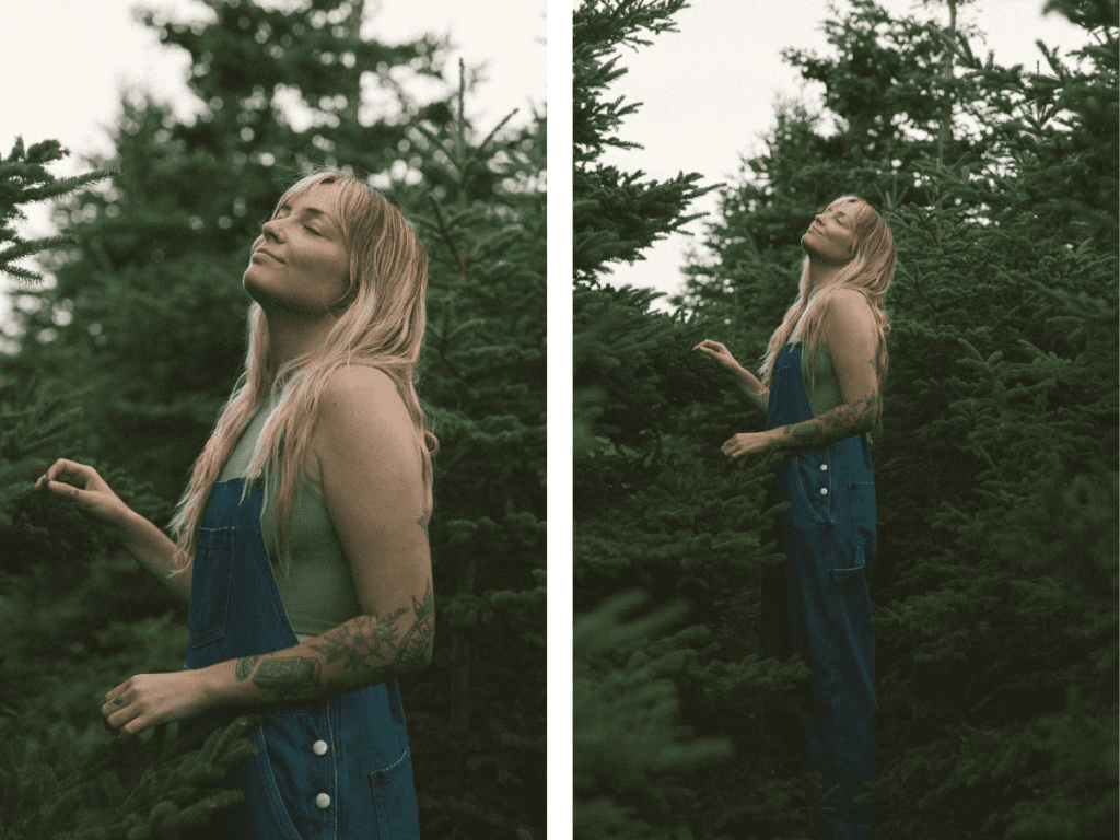 white woman with tattoos closes her eyes and takes a deep breath of the spruce trees she is surrounded by