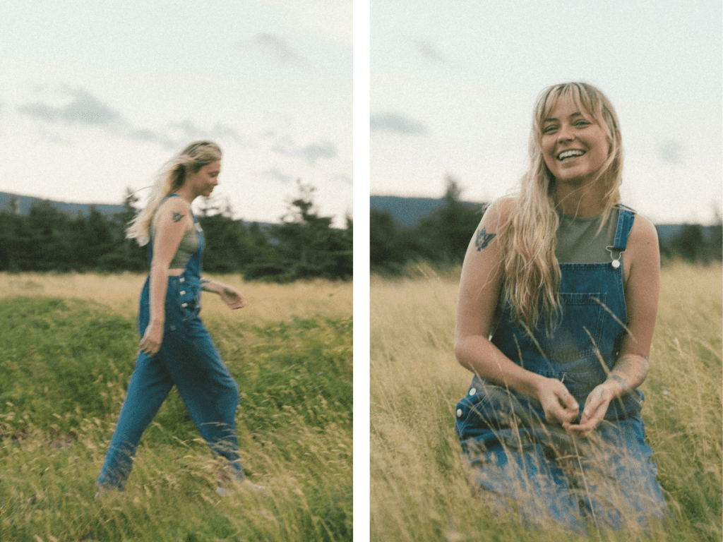 blonde woman with tattoos laughs in a field of tall grass at sunset