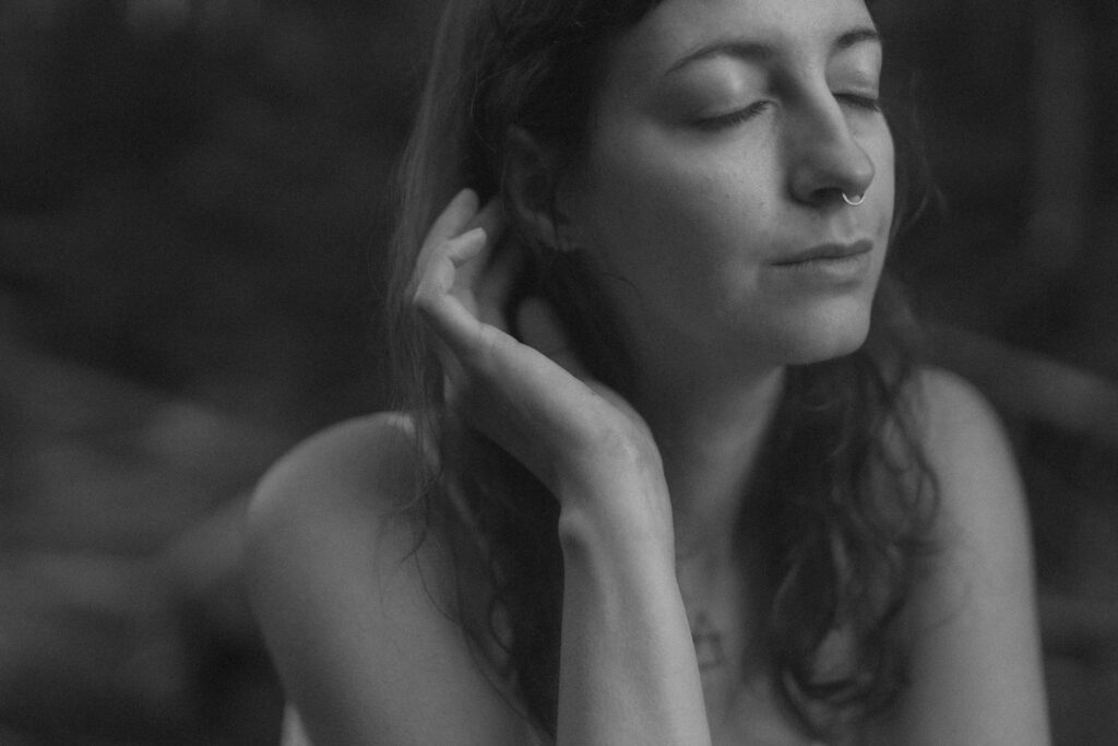 a woman with serenely closed eyes tucks her long dark hair behind her ear.