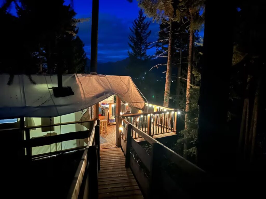 a dark photo of a warmly lit treehouse at night surrounded by tall trees