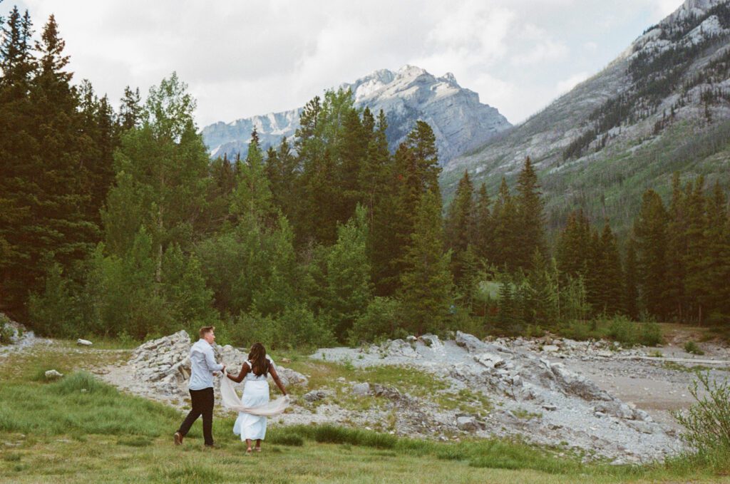 Bride and Groom walk along the rocky shore of Lake Minnewanka in Banff