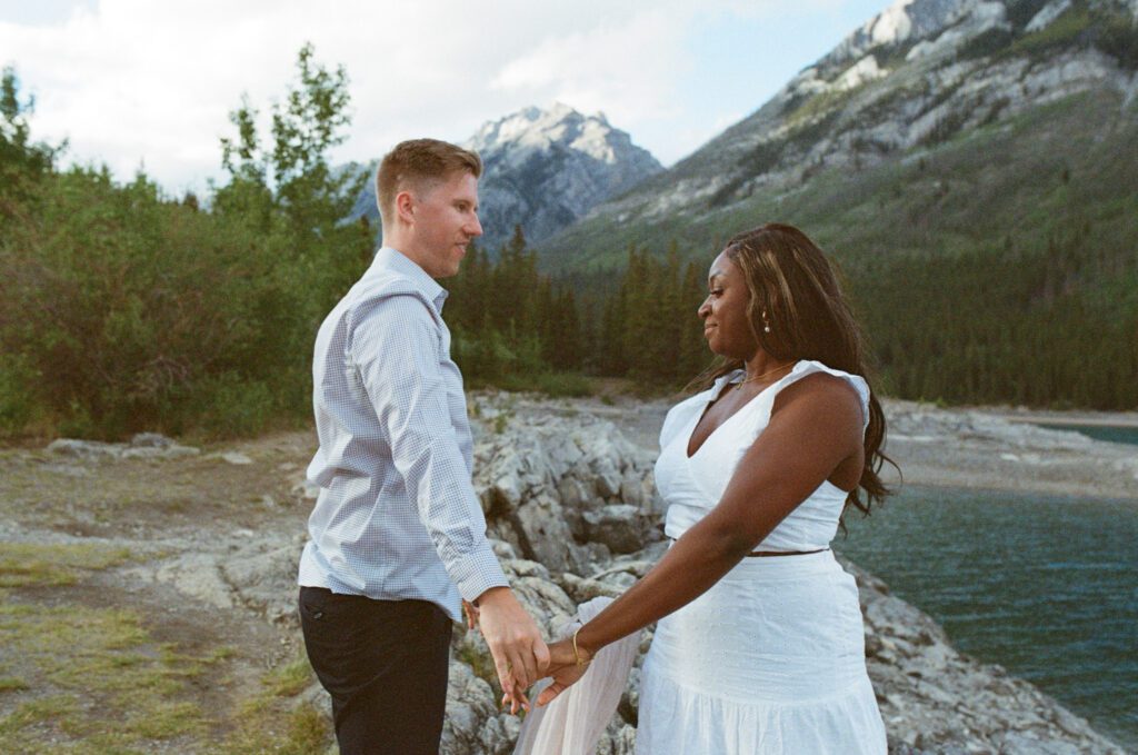 bride and groom hold hands on a rocky outcrop in Banff with mountains all around them