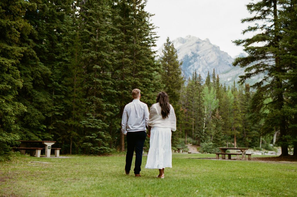 Bride and Groom walk through a lush green campground in Banff National Park