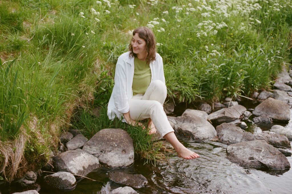 Heather sits on a river in a river with vibrant green grass in the background