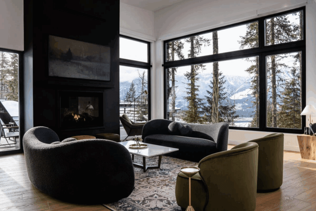 A modern interior with black fireplace and large windows looking out on snowy mountains