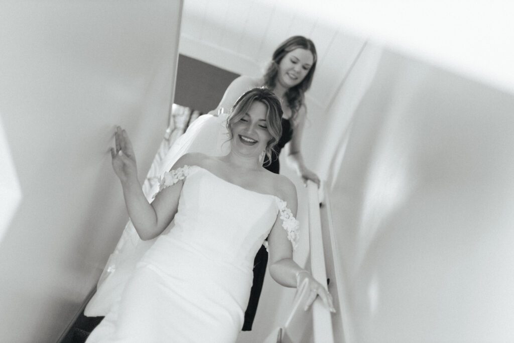 bride's friend holds her train as she walks down the stairs