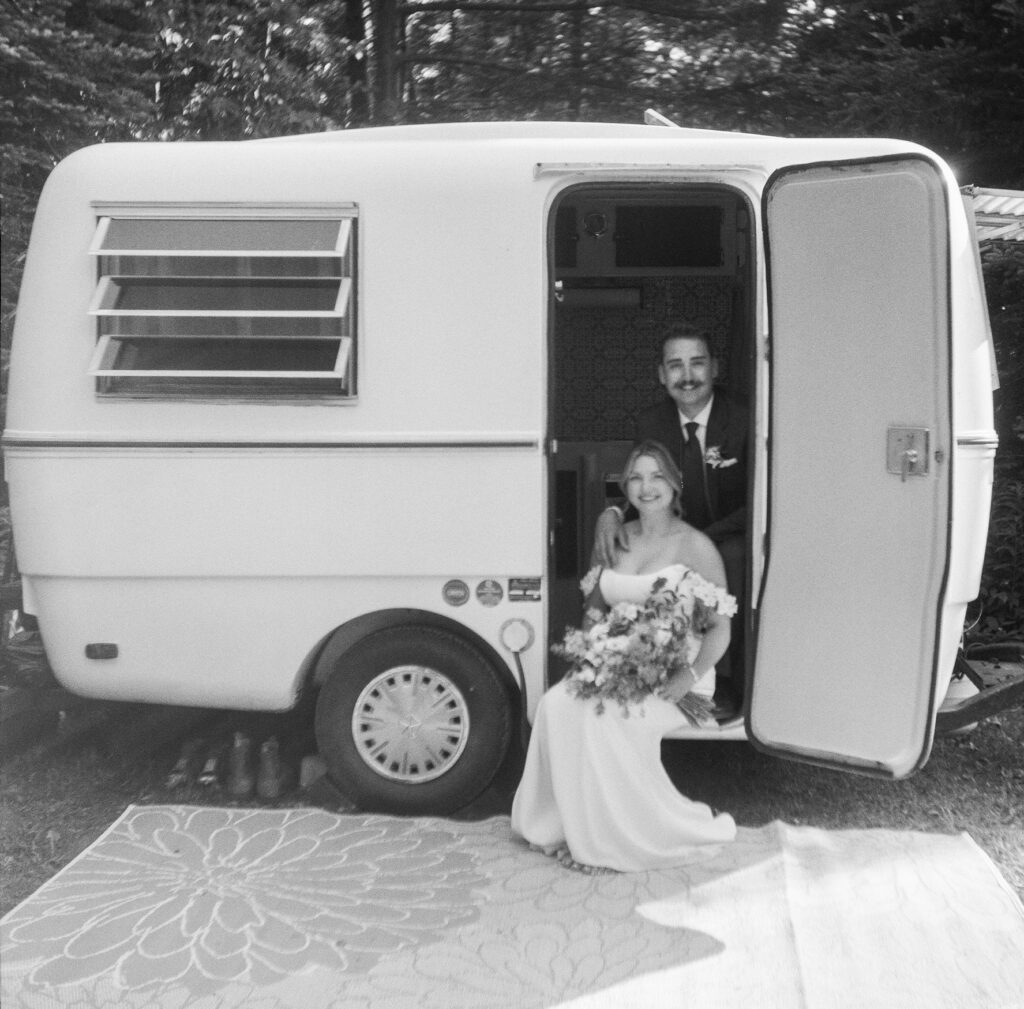 bride and groom sit in the doorway of their 1973 Trillium camper