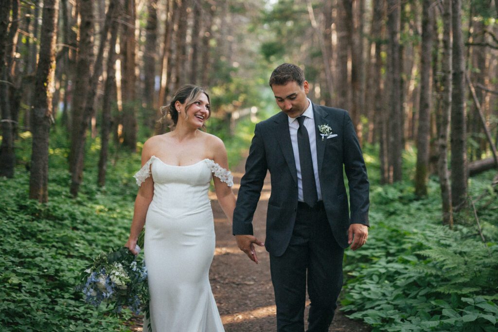 bride and groom laugh as they walk down a forest path