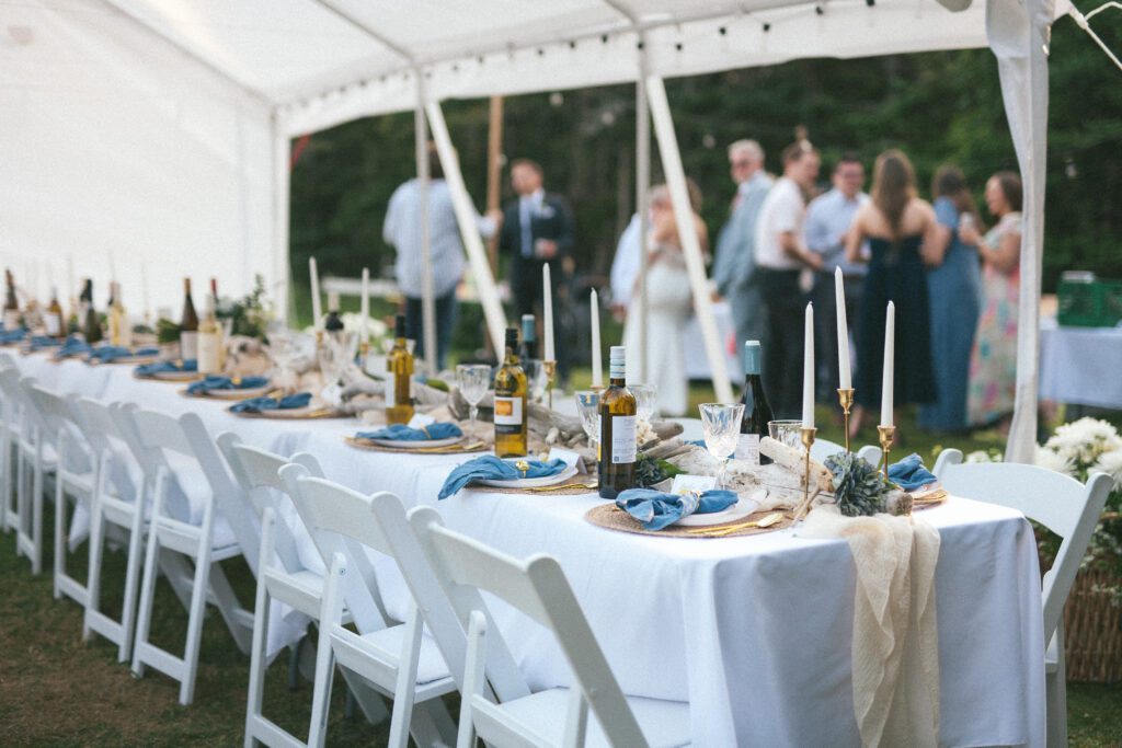 a long table is set beneath a tent with wine, candles, driftwood and beach treasures.