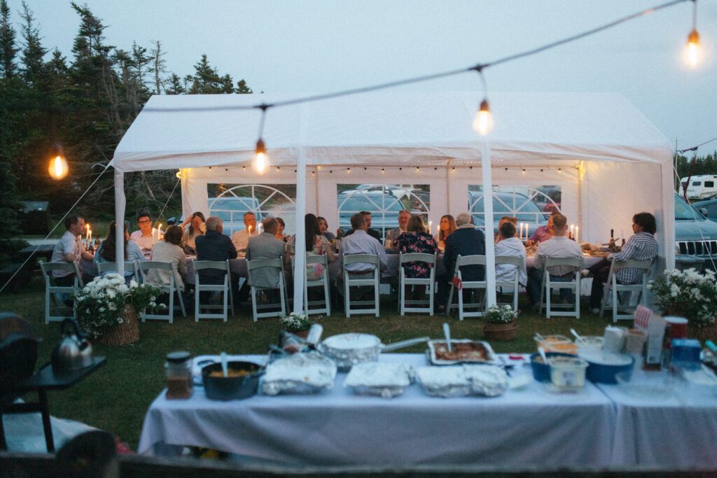 wedding guests sit at long table under tent with warm glow from fairy lights