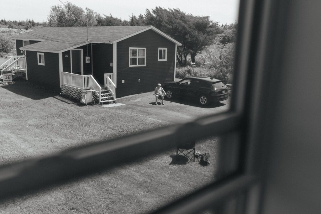 a man sits on a lawn chair in the driveway of a small house