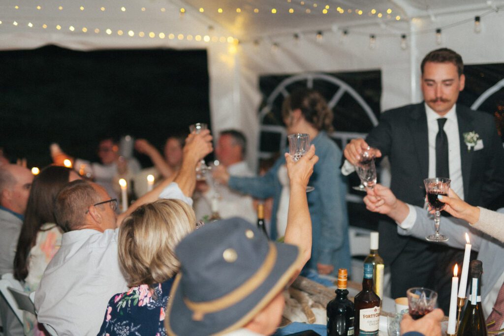wedding guests raise their glasses at long table under tent