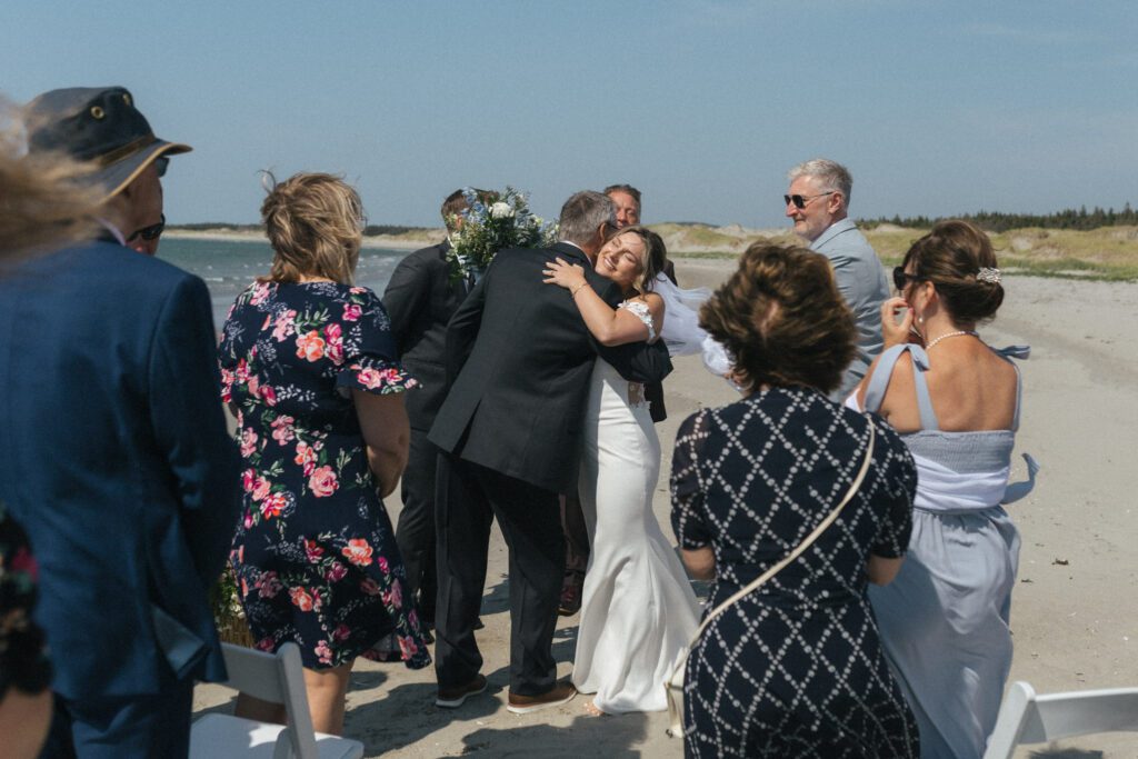 bride hugs her father after walking up the aisle on the beach