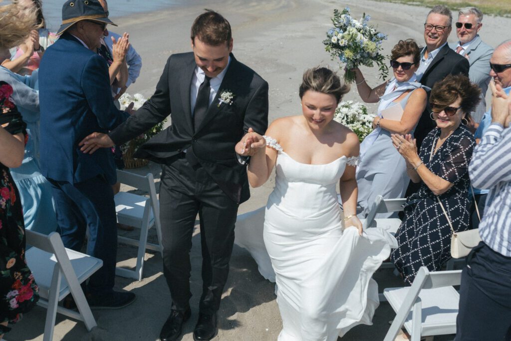 bride and groom walk up the aisle as their families cheer