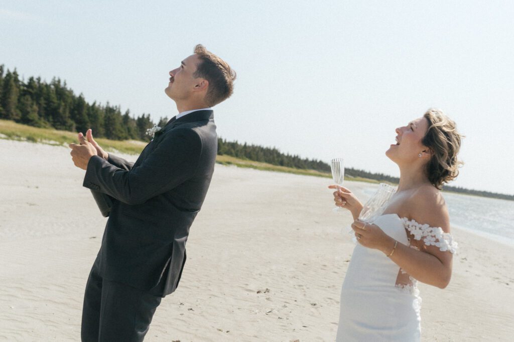 bride cheers while groom pops champagne on the beach