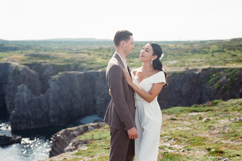 bride and groom hold each other on a green knoll above the ocean