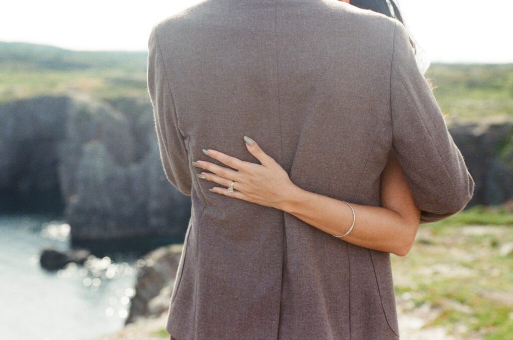 bride's hand with wedding rings on groom's waist 