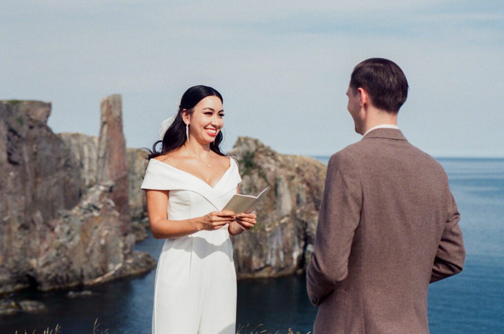 bride grins as she reads her vows above the ocean