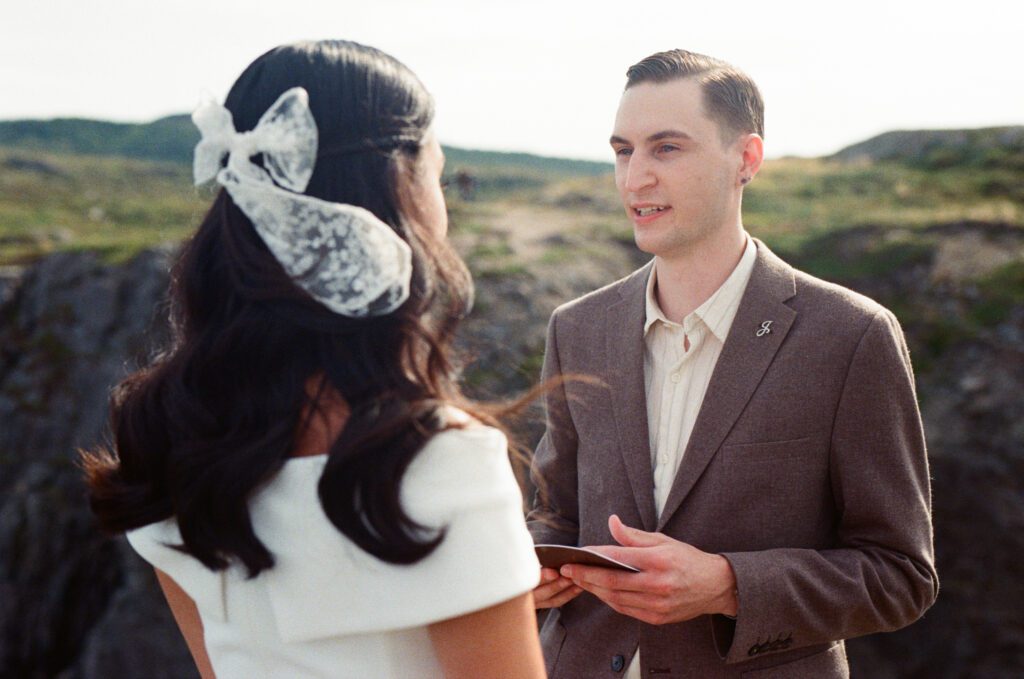 groom reads vows from book to bride, who faces him
