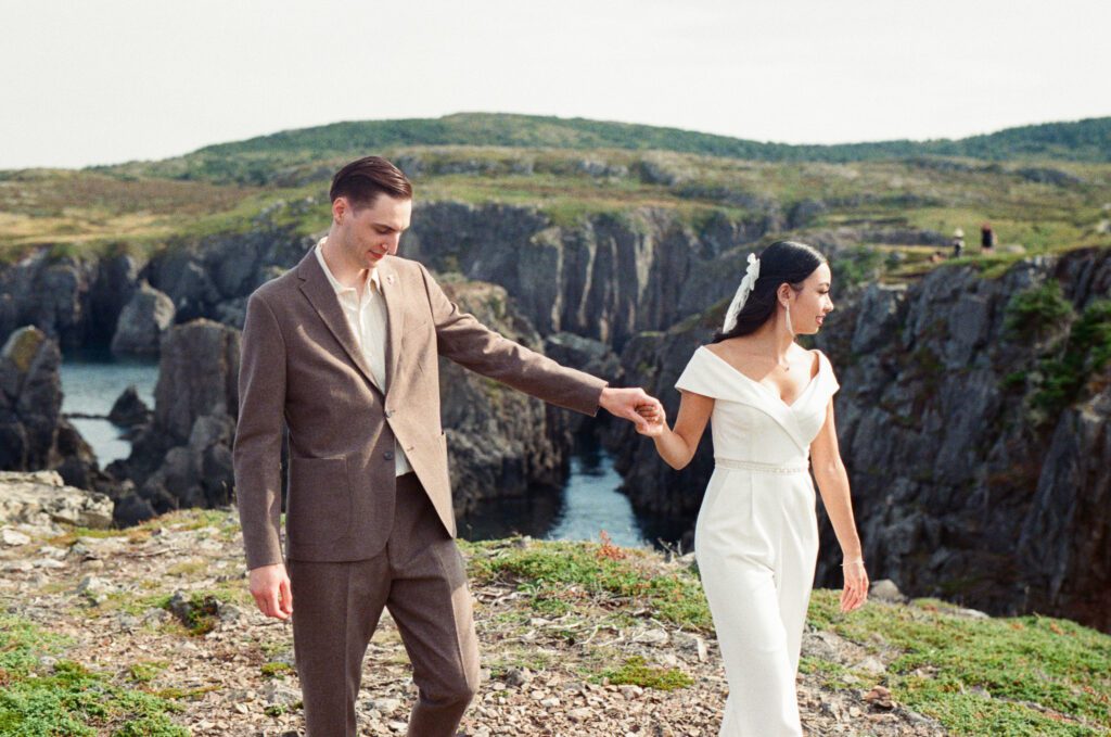 bride and groom hold hands and walk along rocky cliff