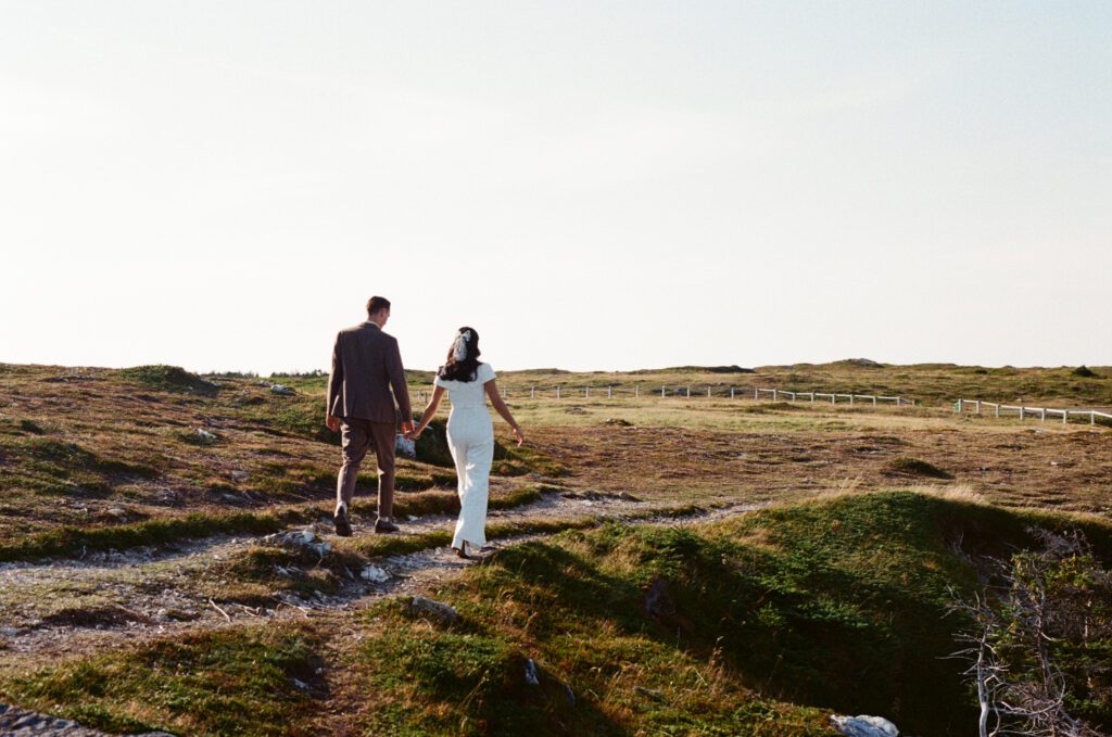 bride and groom walk along a trail in a grassy meadow