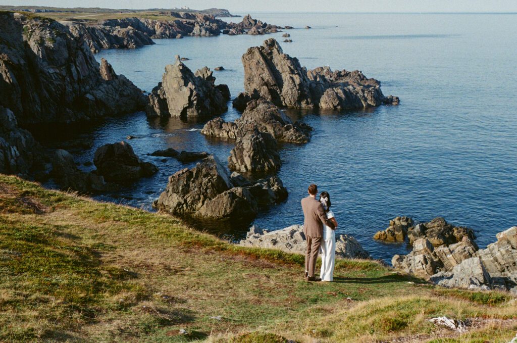 bride and groom hold each other in a meadow overlooking the ocean with sea stacks in the background