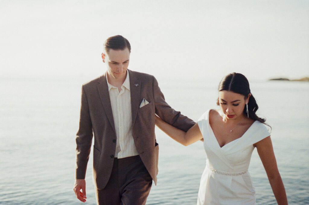 bride and groom walk along the shore beside the ocean