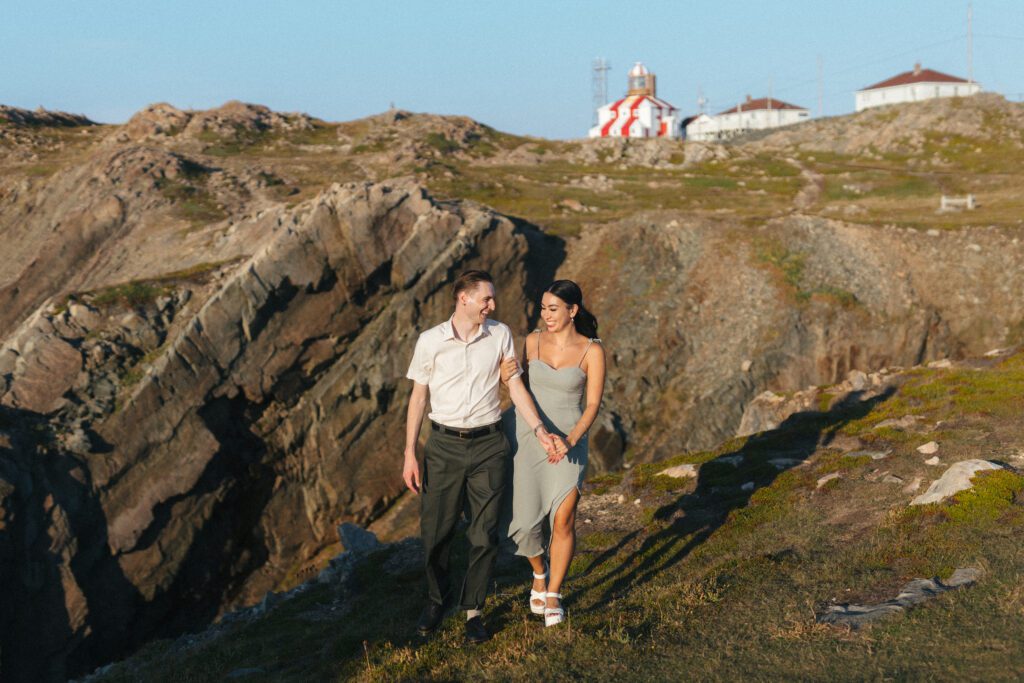 bride and groom walk along rocky cliff in front of the Bonavista Lighthouse