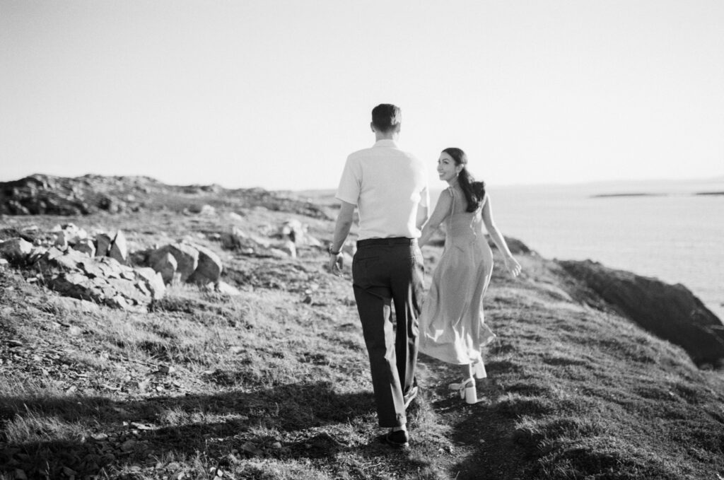 bride and groom laugh and run along trail by the ocean