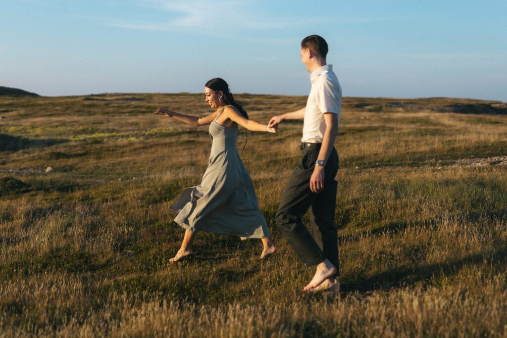 barefoot bride and groom run through a meadow of tall grass
