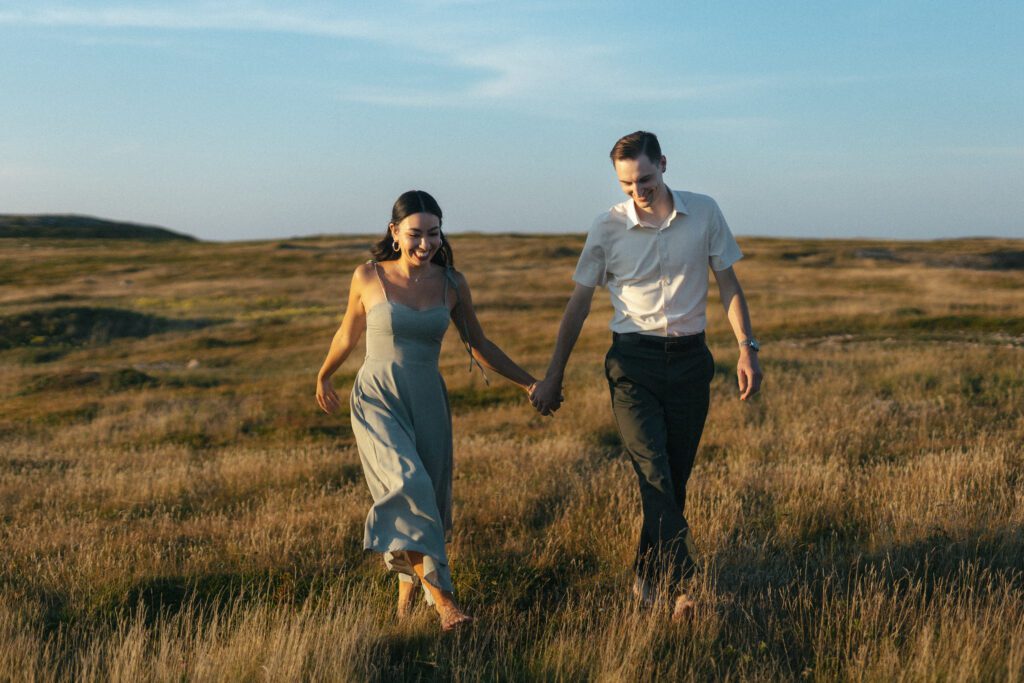 barefoot bride and groom laugh and walk through tall grass
