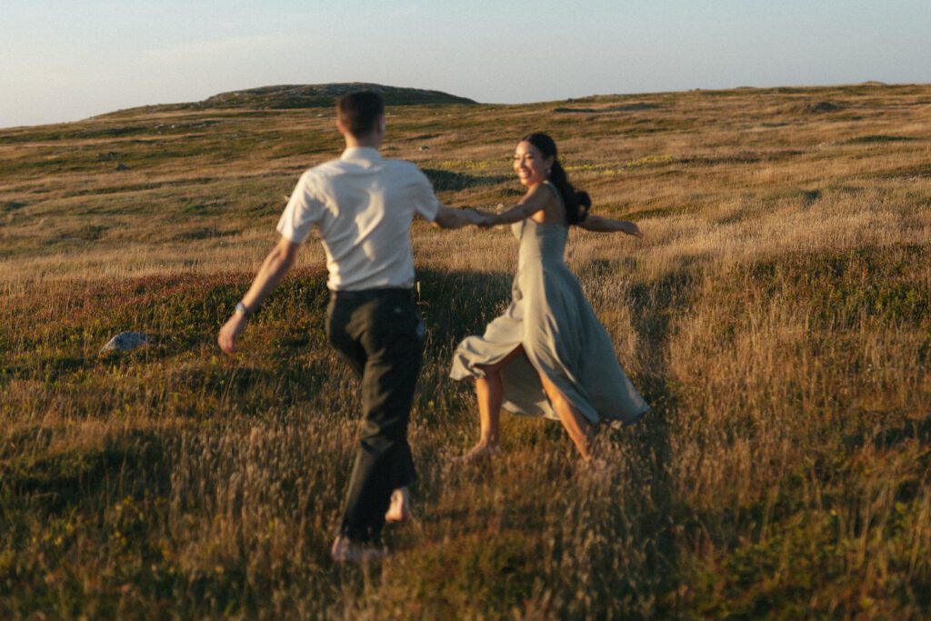 barefoot bride and groom laugh and spin in a field of tall grass