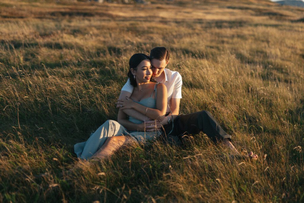 bride and groom cuddle in a field of tall grass at golden hour