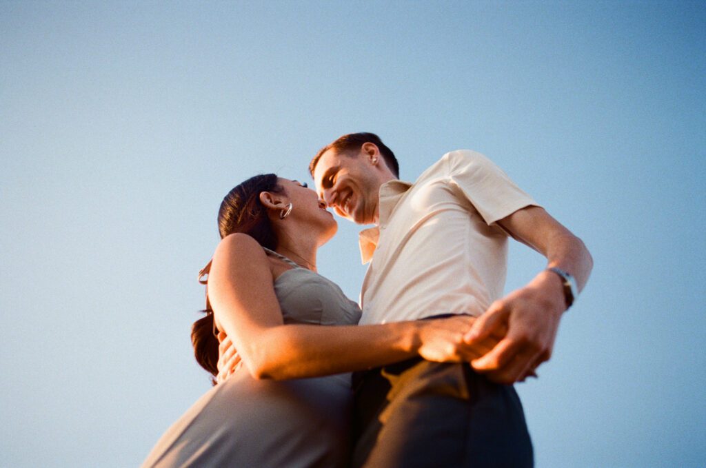 bride and groom laugh and kiss against a blue sky