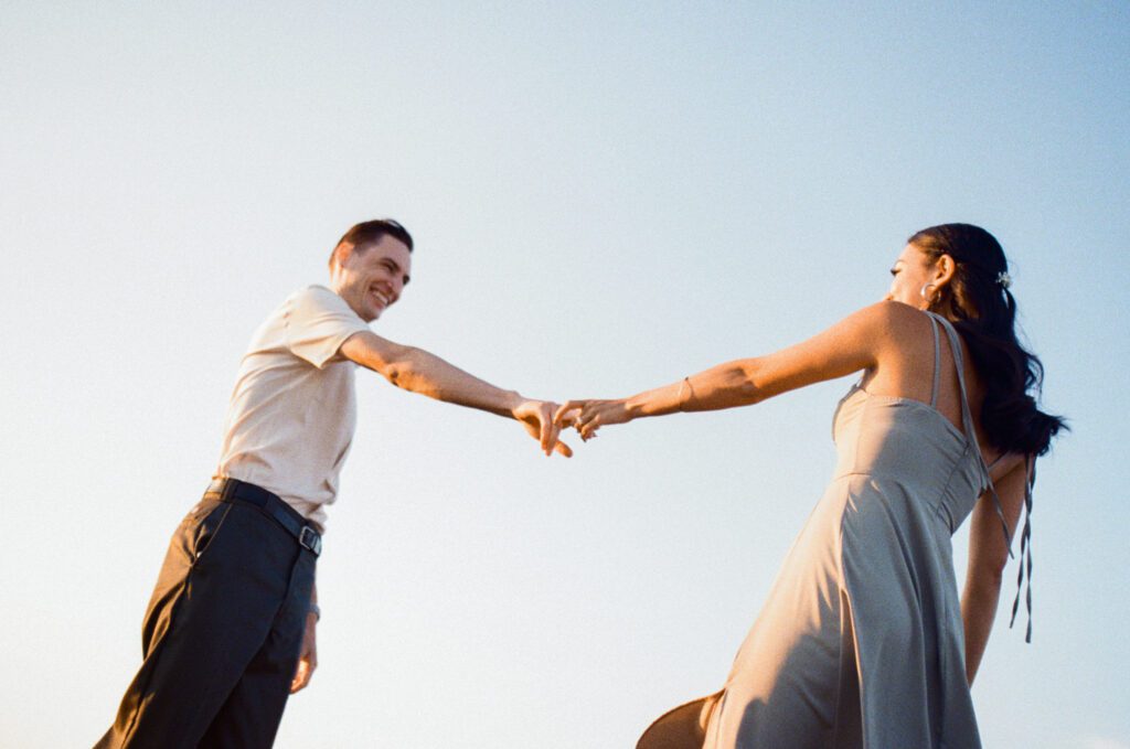 bride and groom laugh and spin around against a blue sky