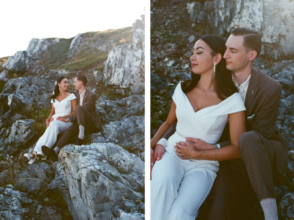 bride and groom hold each other while sitting on a rocky shore