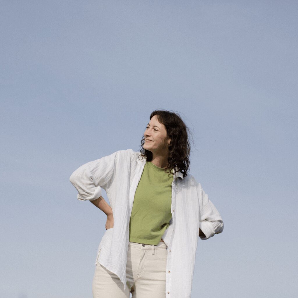 non-binary person laughs and leans to the right against a blue sky
