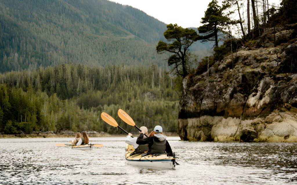 two kayakers paddle along a shore with cliffs